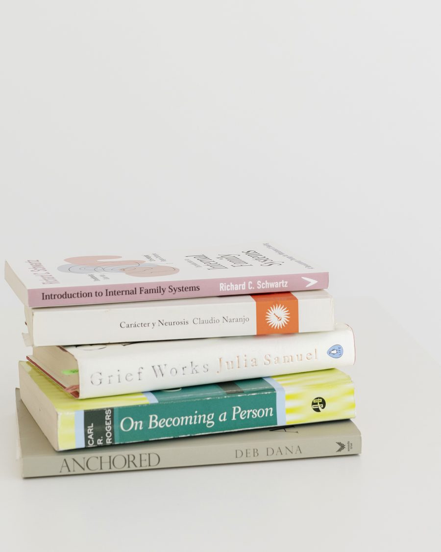 A pile of books on Clara's desk: On Becoming a Person, Grief Works, Anchored, Carácter y Neurosis and Introduction to Internal Family Systems