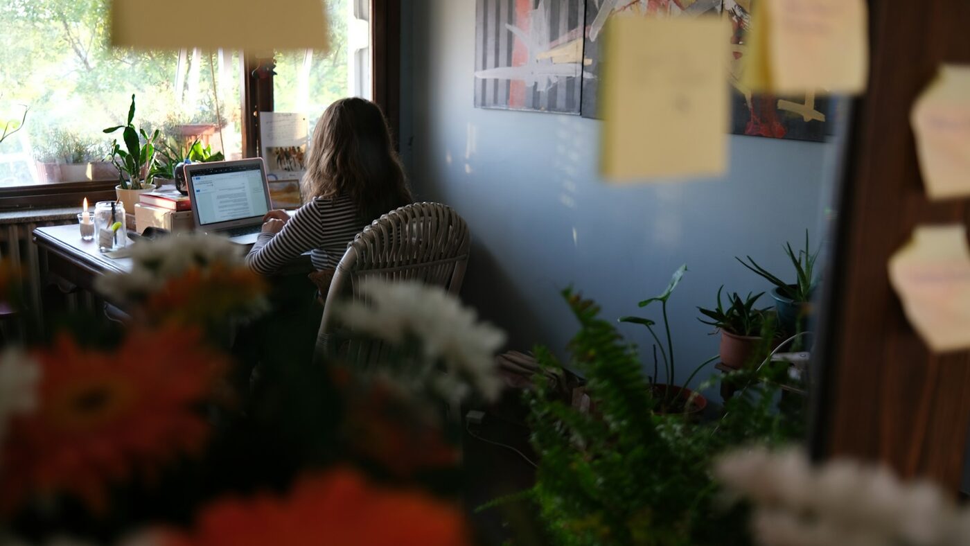 Someone working alone on a laptop at a desk by a window at home